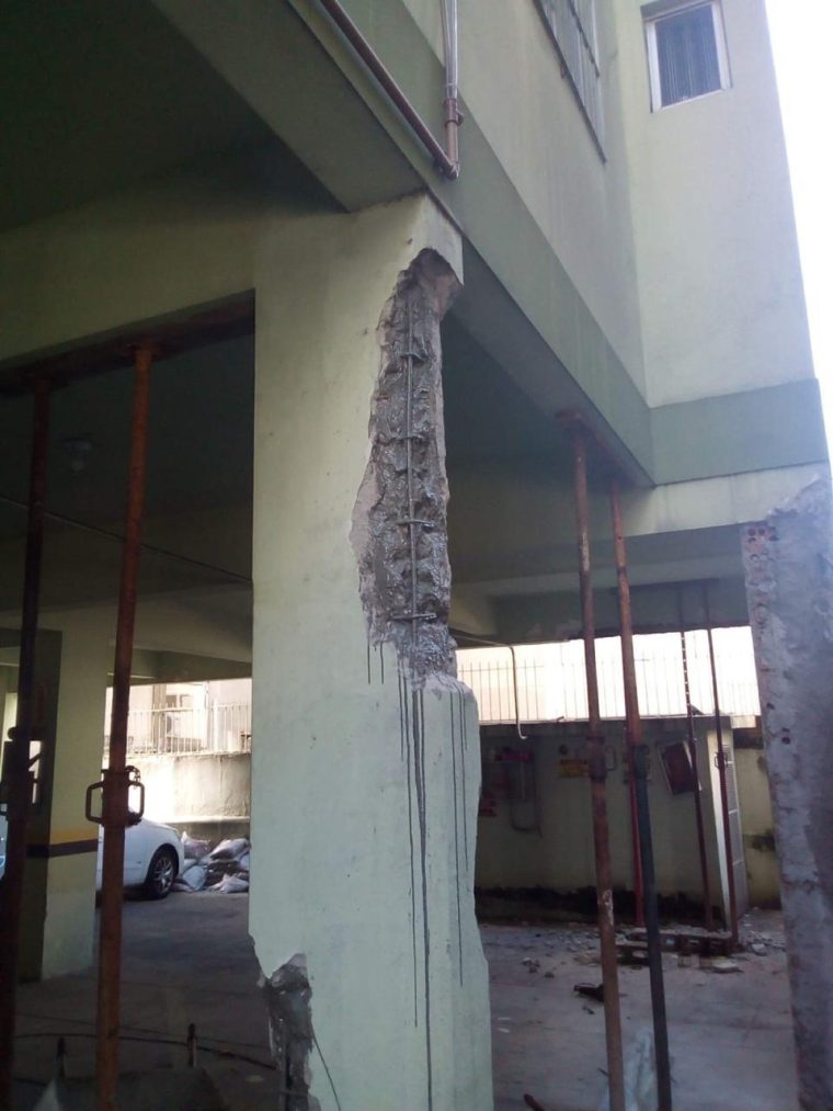 Pilar de pilotis com o concreto removido em toda a altura, armadura exposta e escoramento metálico ao redor