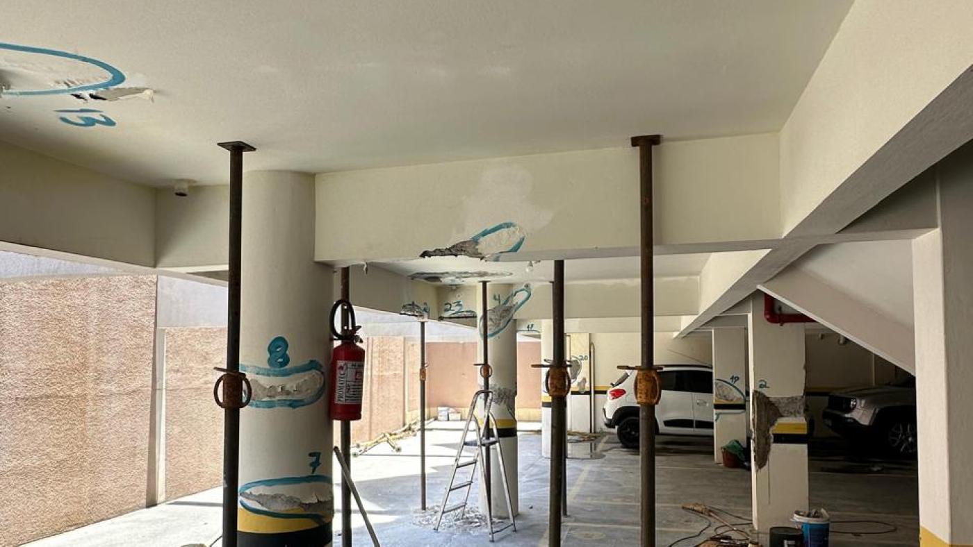Garagem de condomínio escorada, com pontos de patologia estrutural marcados a giz no teto e nos pilares