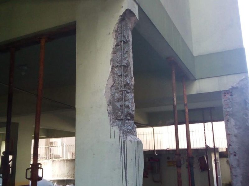 Pilar de pilotis aberto verticalmente com armadura à mostra e escoras metálicas apoiando a estrutura ao redor