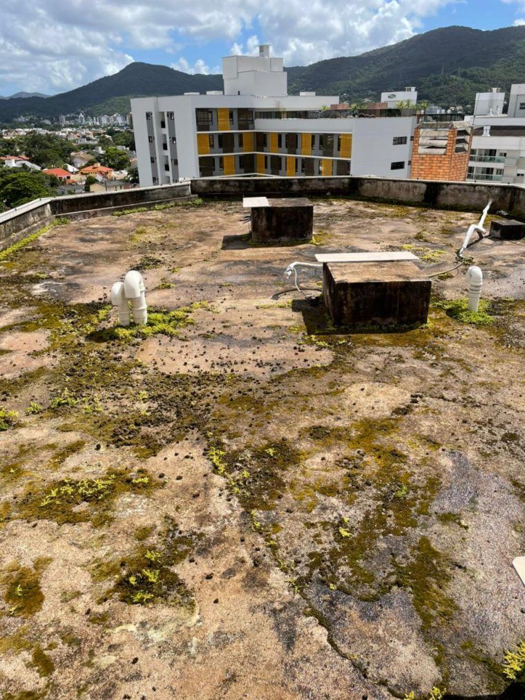 Laje de cobertura de condomínio com a superfície desgastada, manchas de musgo seco e água empoçada