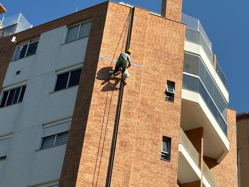 Profissional descendo por corda na empena de tijolo à vista de um edifício residencial