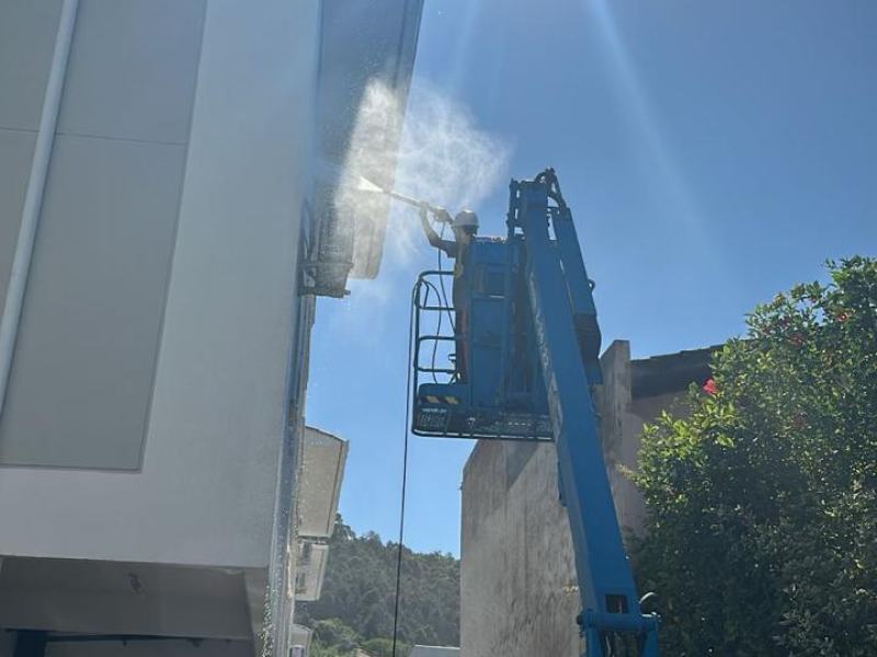 Operário em plataforma elevatória lavando a fachada de um edifício com jato de água
