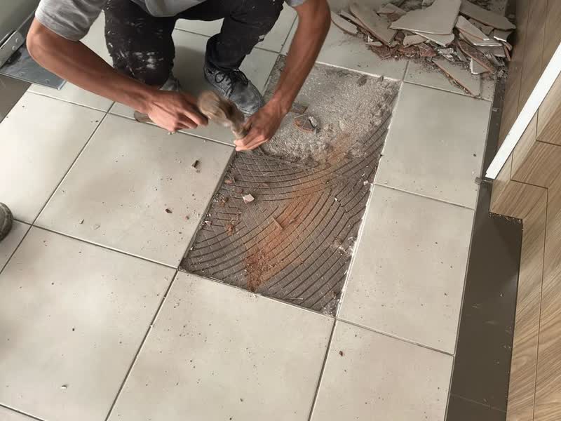 Operário removendo com talhadeira o piso cerâmico antigo do hall de um condomínio